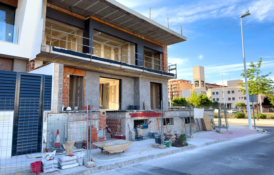 Chantier de construction ext&eacute;rieur avec contrema&icirc;tre en casque blanc et chemise &agrave; carreaux consultant des plans ou documents