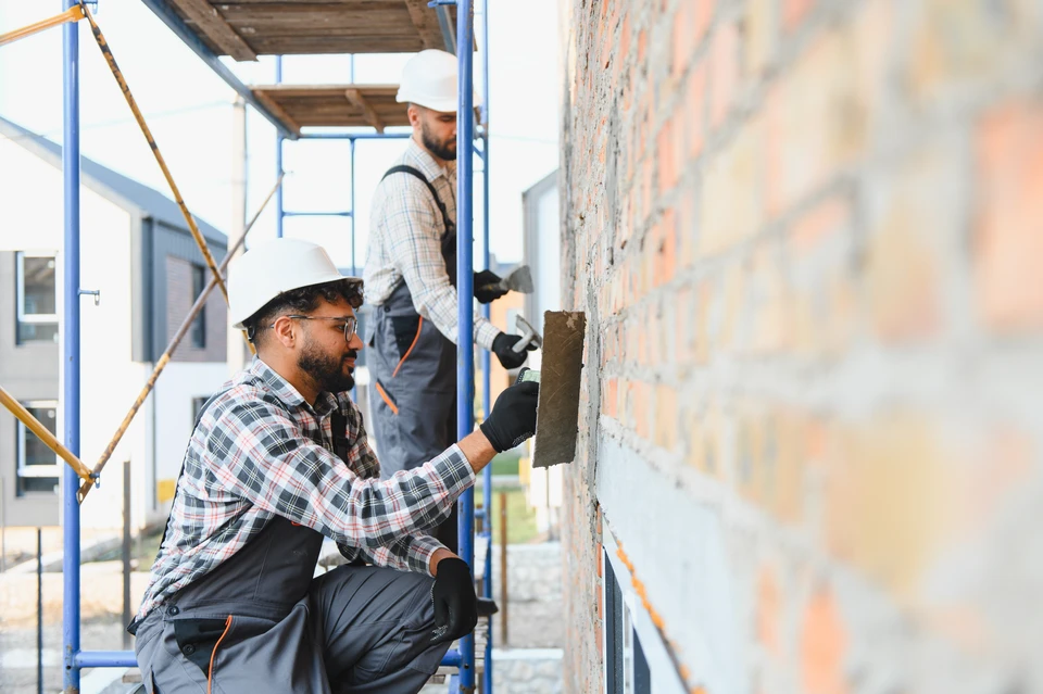Deux professionnels du bâtiment en casques de chantier jaune et blanc examinent un chantier de construction, l'un pointant vers une structure en béton armé