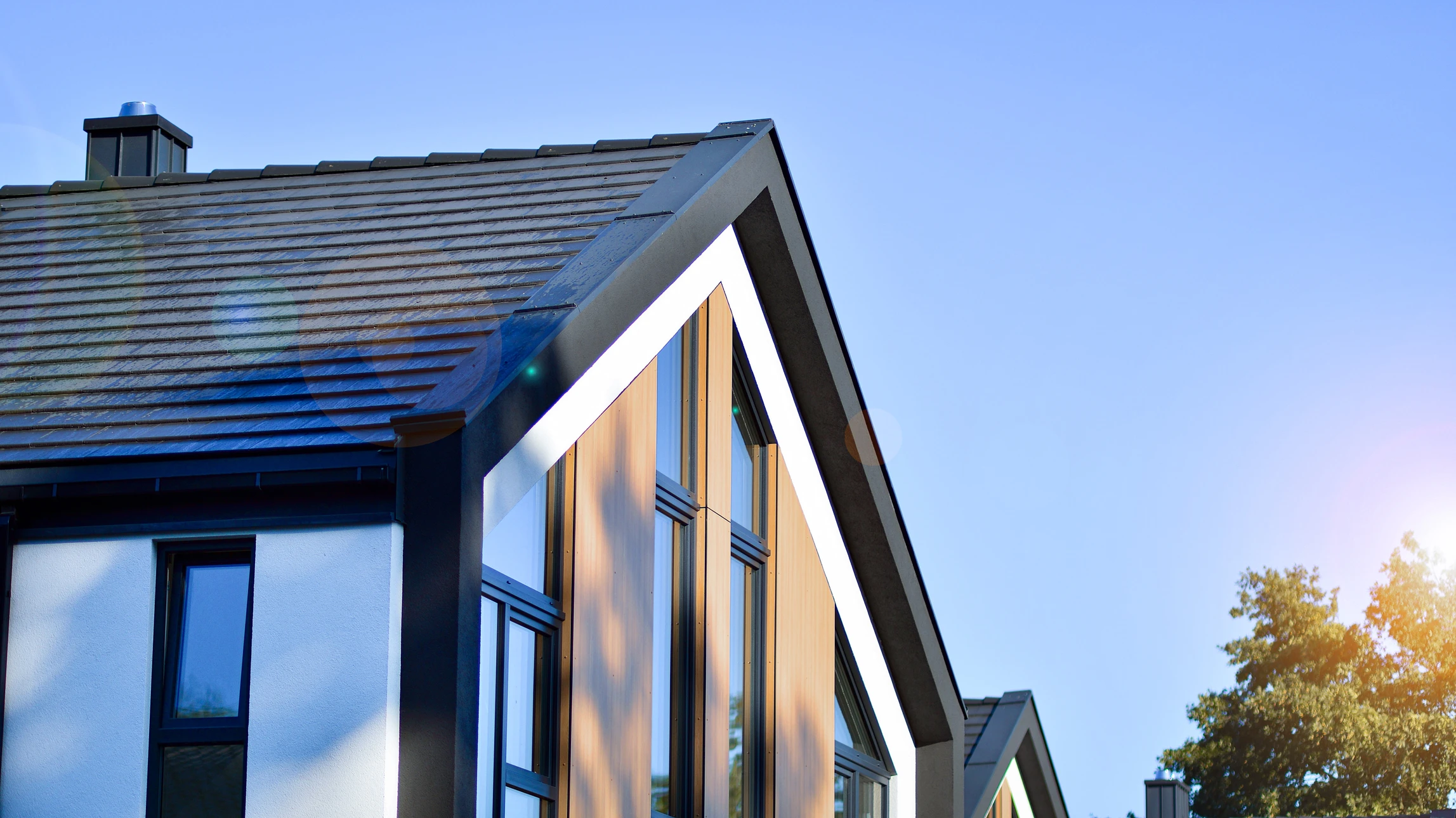 Maison individuelle contemporaine en brique beige avec toiture tuiles grises, garage double porte sectionnelle blanche, pelouse verte entretenue, aménagement paysager avec arbustes, allée béton lissé, boîte aux lettres maçonnée assortie